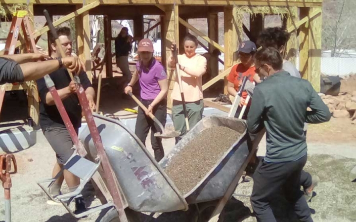 A group of students use shovels and wheelbarrows as they participate in a service project with outward bound